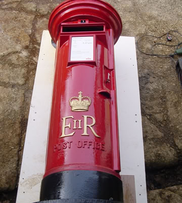 A red cylindrical post box with a black base and top, featuring a crown symbol and the letters "E II R" on the front.
