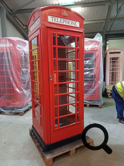 A red British-style telephone booth with an open door, revealing a white interior door inside.