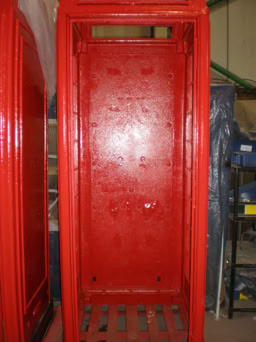Red telephone booth interior with visible walls and floor, no phone equipment present.