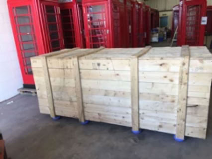 Wooden crates on a warehouse floor with red phone booths in the background.