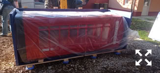A large red object wrapped in transparent plastic, placed on a wooden pallet outdoors.