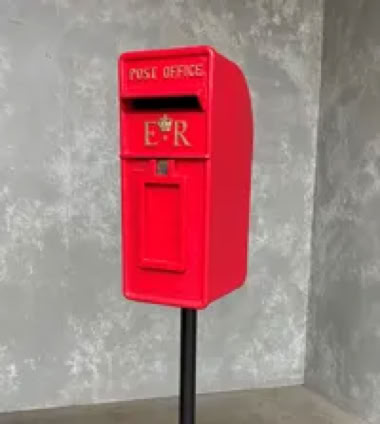 A red post box mounted on a black stand against a gray textured wall.